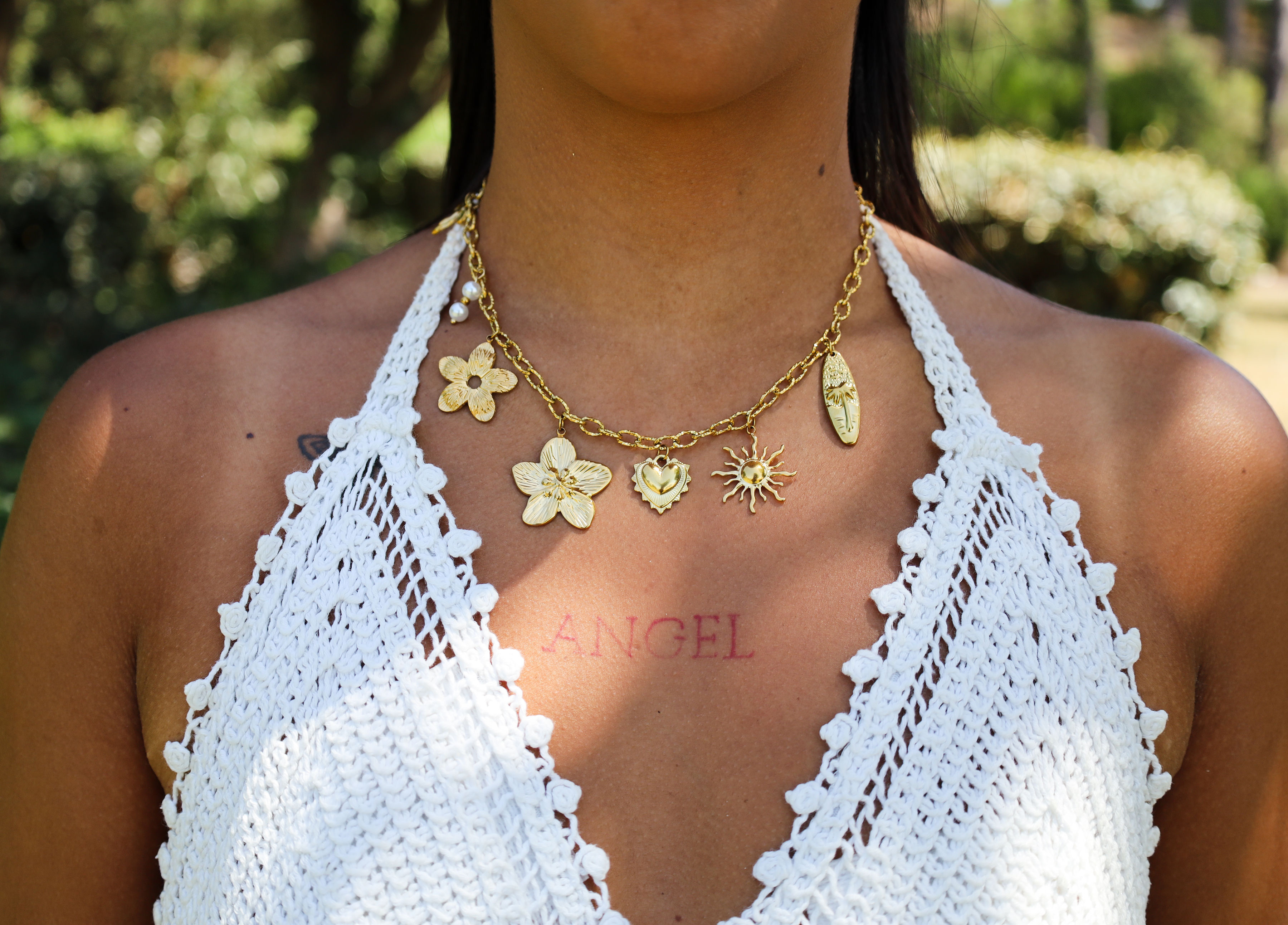 Femme portant un collier doré à charms dans un jardin ensoleillé — L'Atelier de Nana